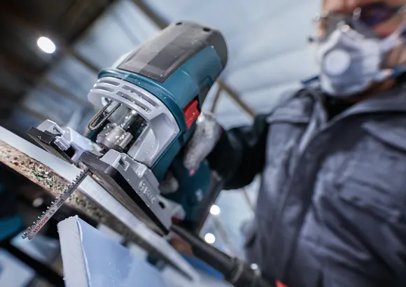 Una persona que usa equipo de seguridad utiliza una sierra caladora para cortar un trozo de material.