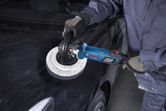 Una persona que usa equipo de seguridad utiliza una pulidora en el capó de un automóvil negro.