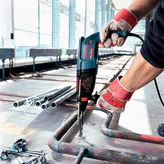 Una persona que usa equipo de seguridad perfora una tubería de metal en un sitio de construcción.