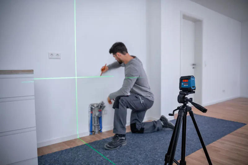 Una persona se arrodilla y marca una pared utilizando un nivel láser.