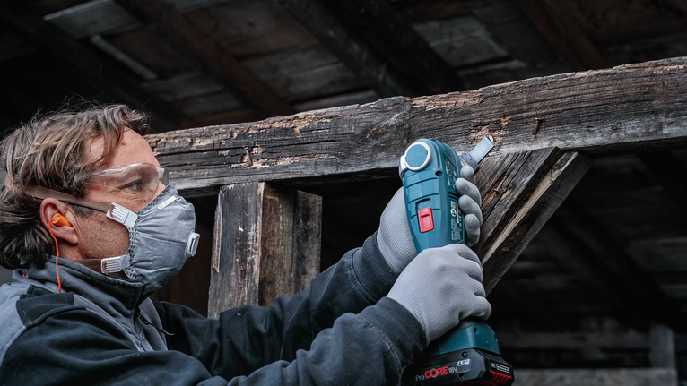 Una persona que usa equipo de seguridad utiliza una herramienta inalámbrica para lijar madera desgastada.