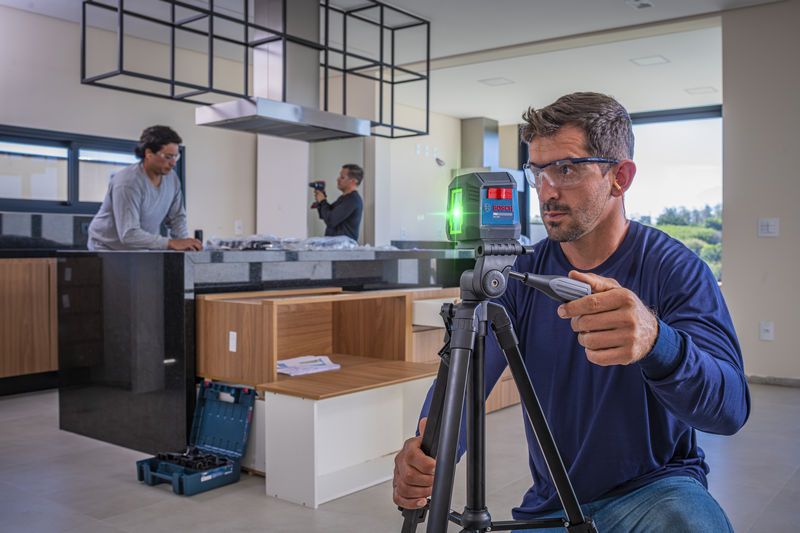Un trabajador equipado con equipo de seguridad ajusta una herramienta de nivelación láser sobre un trípode en una cocina moderna.