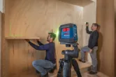 Dos personas con equipo de seguridad utilizan una herramienta de nivelación láser para instalar estantes.