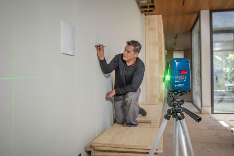 Una persona marca una pared utilizando un nivel láser que proyecta líneas verdes.