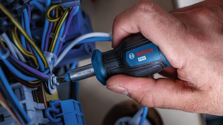 Una persona aprieta un tornillo entre los cables eléctricos con un destornillador.