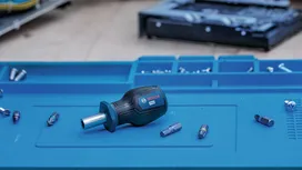 Destornillador manual y puntas variadas colocados sobre una superficie de trabajo azul.