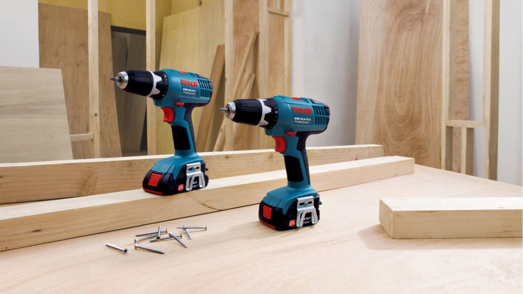 Dos taladros Bosch Professional sobre una mesa de trabajo con tornillos y madera.