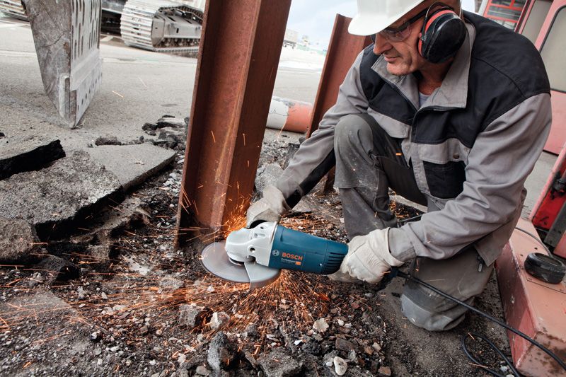 Un trabajador que usa equipo de seguridad utiliza una amoladora angular para cortar metal, lo que produce chispas.