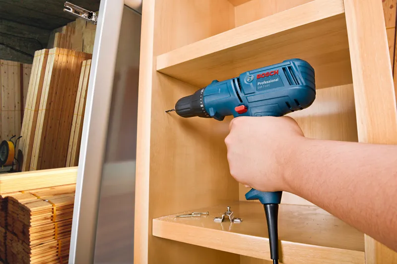 Una persona perfora un agujero en un armario de madera utilizando un taladro.