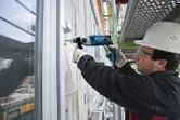 Una persona que usa equipo de seguridad perfora una pared de hormigón en una obra en construcción.