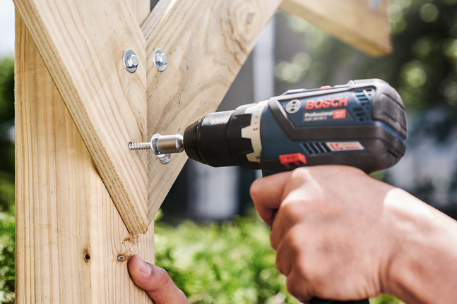 Persona atornillando un tornillo en madera con un taladro inalámbrico.