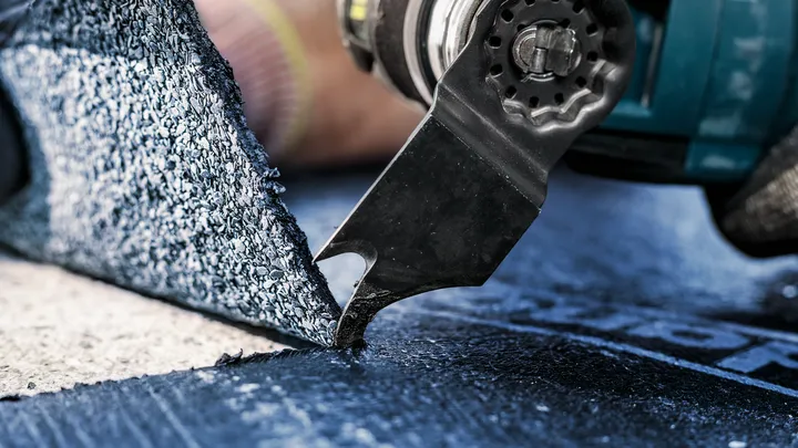 Una persona que usa equipo de seguridad utiliza una herramienta eléctrica para cortar material de piso.