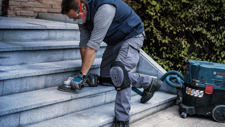 Una persona que usa equipo de seguridad pule escaleras de piedra con una herramienta eléctrica.