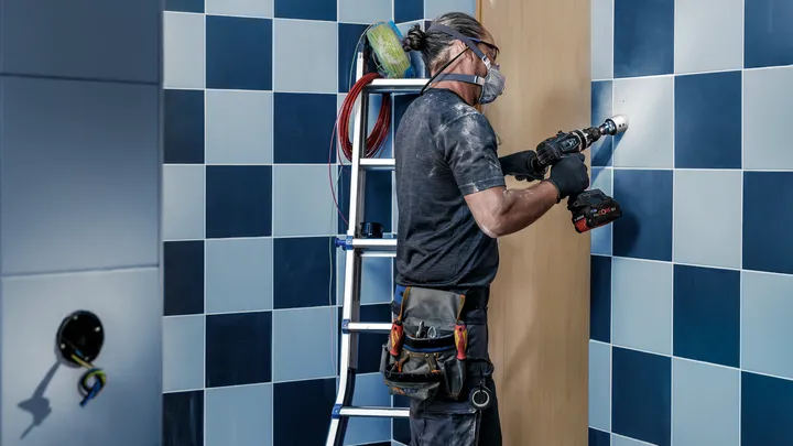 Una persona que usa equipo de seguridad perfora un agujero en una pared de azulejos.