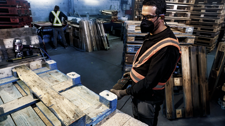 Una persona que usa equipo de seguridad utiliza una herramienta eléctrica para trabajar sobre una paleta de madera.