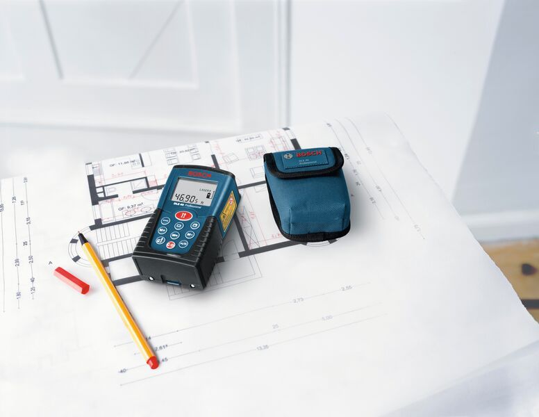 Medidor láser, estuche, lápiz y tapa colocados sobre planos arquitectónicos.