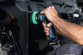 Una persona utiliza una pulidora inalámbrica para pulir la superficie de la puerta de un automóvil negro.