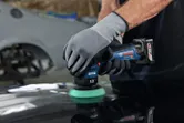 Una persona que usa equipo de seguridad pule la superficie de un automóvil con una pulidora inalámbrica.