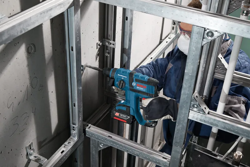 Una persona que usa equipo de seguridad perfora una pared de hormigón utilizando un martillo perforador inalámbrico.