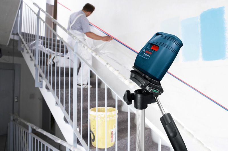 Laser leveling tool projects lines on a stairway wall while a person prepares the surface.