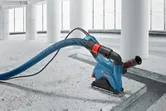 Wall chaser with dust extraction hose is cutting a groove in a concrete floor.