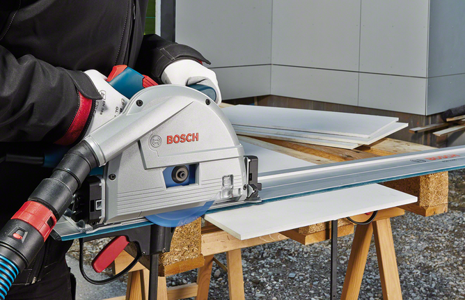 A person wearing safety equipment cuts a sheet with a circular saw on a workbench.