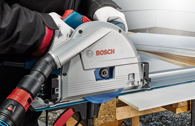 Person wearing safety equipment cuts a panel with a circular saw on a workbench.