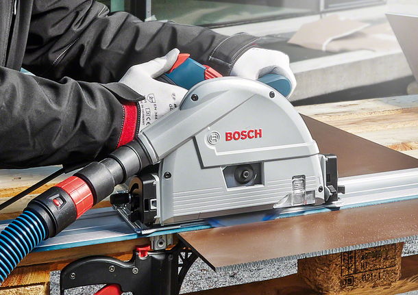 Person wearing safety equipment uses a track saw to cut a sheet of material.
