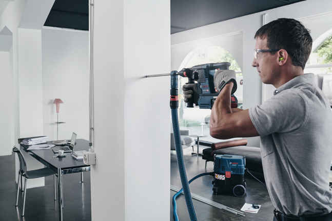 A worker wearing safety equipment drills into a white wall in a modern office.