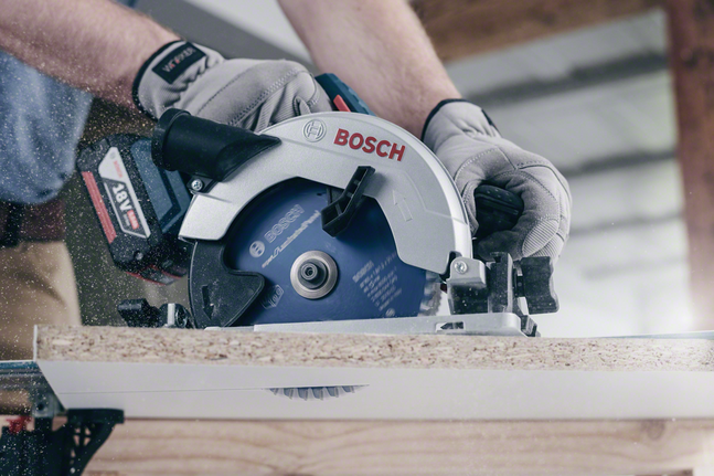 Person wearing safety equipment cuts particle board with a circular saw.