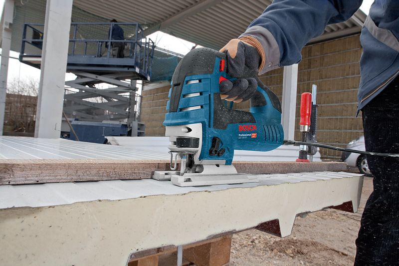 Person wearing safety equipment uses a jigsaw to cut a panel outdoors.