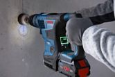 A person wearing safety equipment drills a hole into concrete with a cordless rotary hammer.