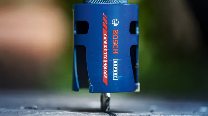 Close-up of a blue carbide hole saw drilling into a flat surface.