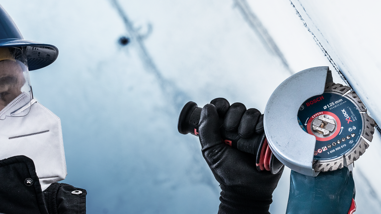 A person wearing safety equipment uses an angle grinder to cut a metal surface.