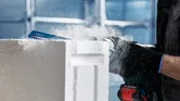 Person wearing safety equipment cuts a concrete block with a power tool.