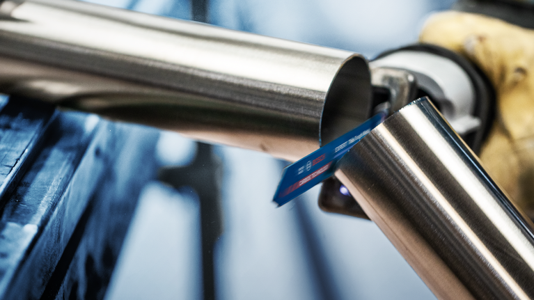 Person wearing safety equipment cuts a metal pipe with a reciprocating saw.
