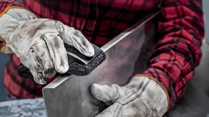 Person wearing safety equipment smooths the edge of a metal sheet.