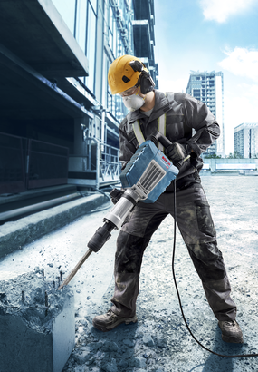 Person wearing safety equipment operates a demolition hammer to break up concrete.