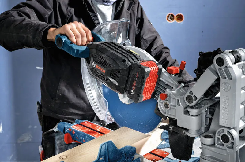 A person wearing safety equipment uses a miter saw with an 8.0Ah battery pack to cut wood.