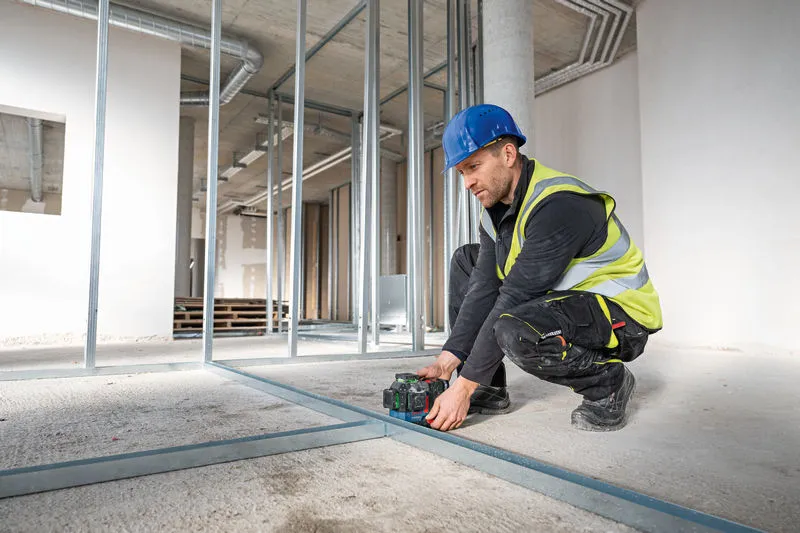 Person wearing safety equipment aligns floor track with a laser leveling tool.