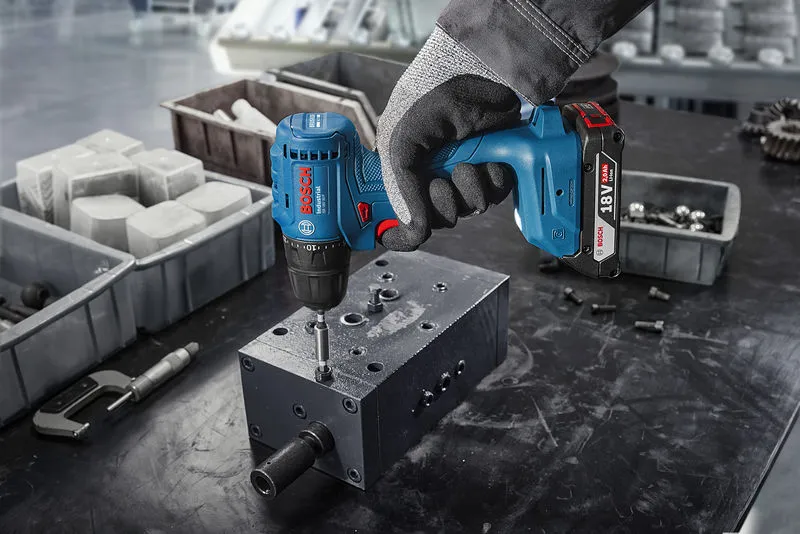 A person wearing safety equipment uses a cordless drill to fasten a screw into metal.