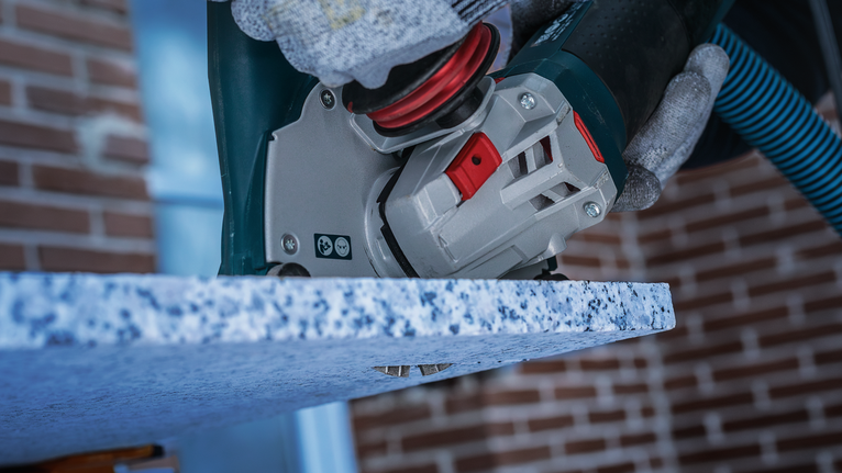 Person wearing safety equipment polishes the edge of a granite countertop.
