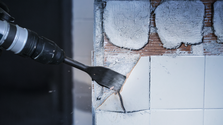 Power tool with chisel attachment removing ceramic tiles from a wall.