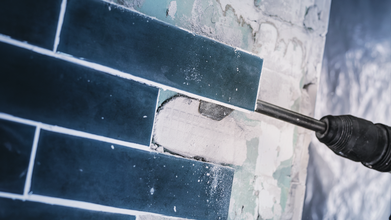 Power tool chipping blue tiles from a wall.