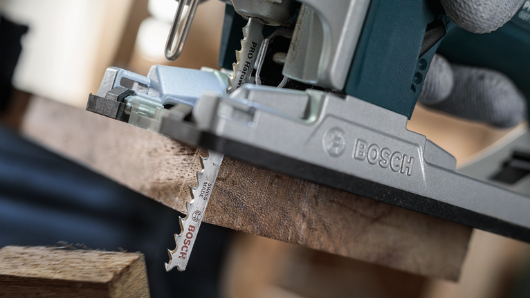 Person wearing safety equipment uses a jigsaw to cut a wooden board.
