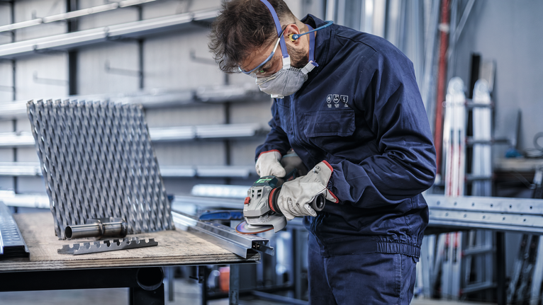 A person wearing safety equipment grinds the edge of a metal beam.