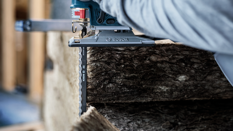 Person wearing safety equipment uses a jigsaw to cut through thick insulation material.