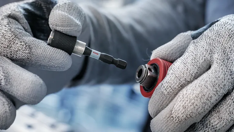 Person wearing safety equipment inserts a screwdriver bit into a drill chuck.