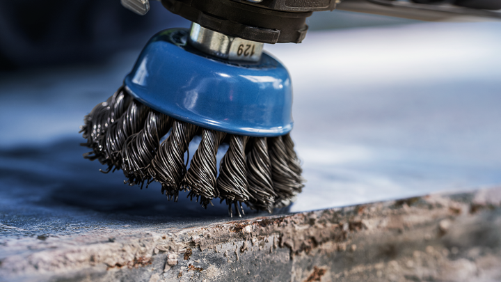 Wire brush tool grinding rust from a metal surface.
