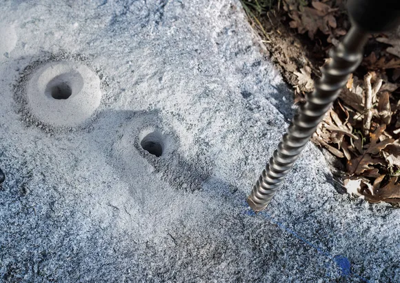 Rotary hammer bit drilling deep holes into a stone surface outdoors.